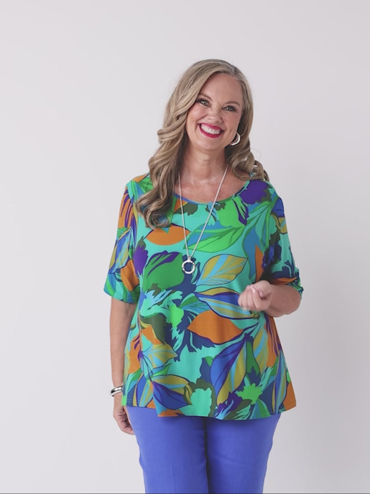 video of model wearing a short-sleeve top with a bold tropical leaf print in green, blue, and orange