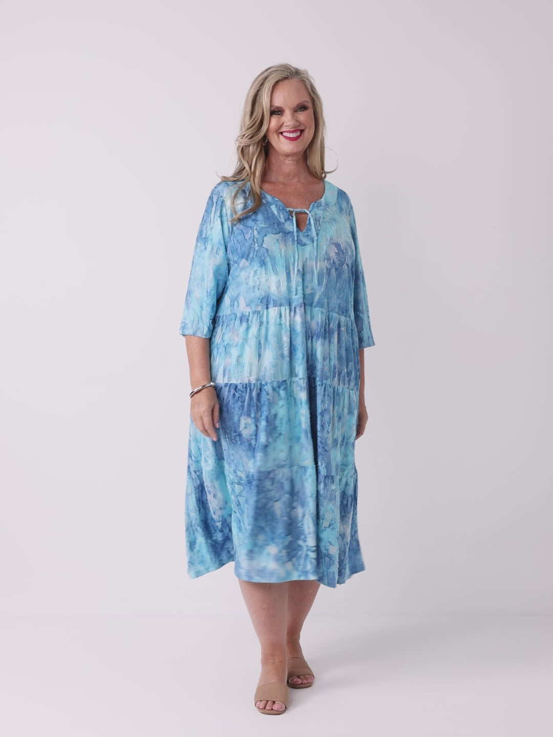 A woman wearing a aqua blue tie die tiered midi dress with tie front v-neckline