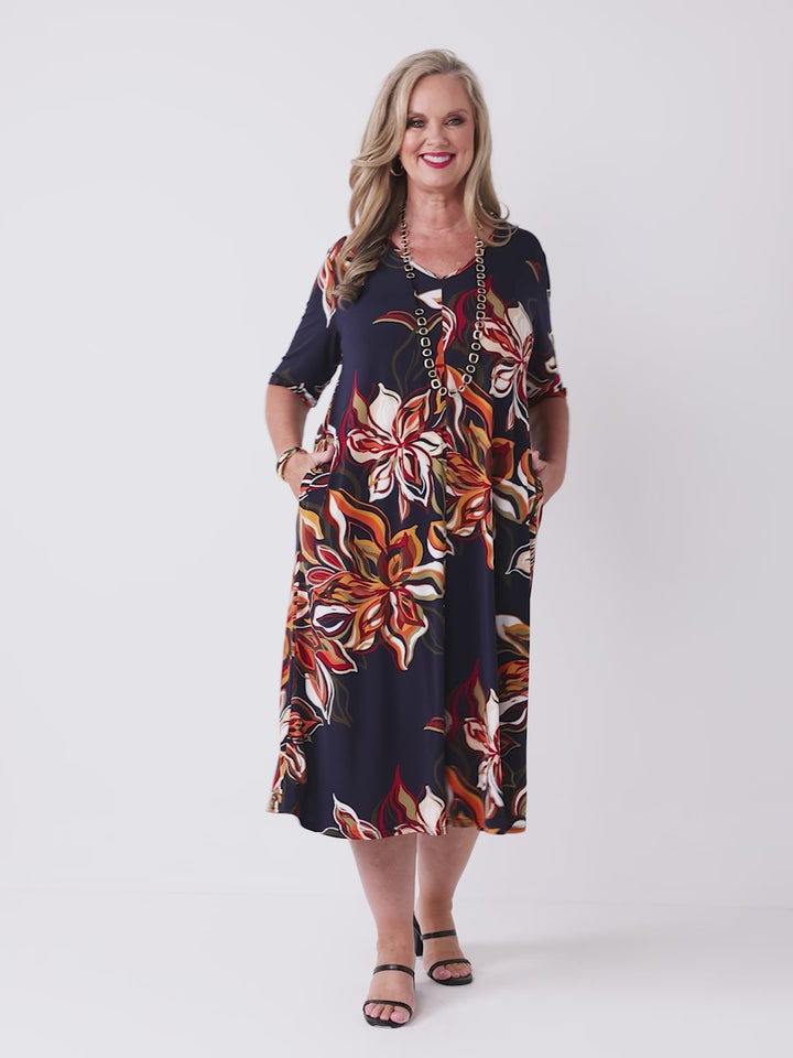 a video of a model wearing a short-sleeve midi dress with a navy blue base and a vibrant orange, red, and white floral print