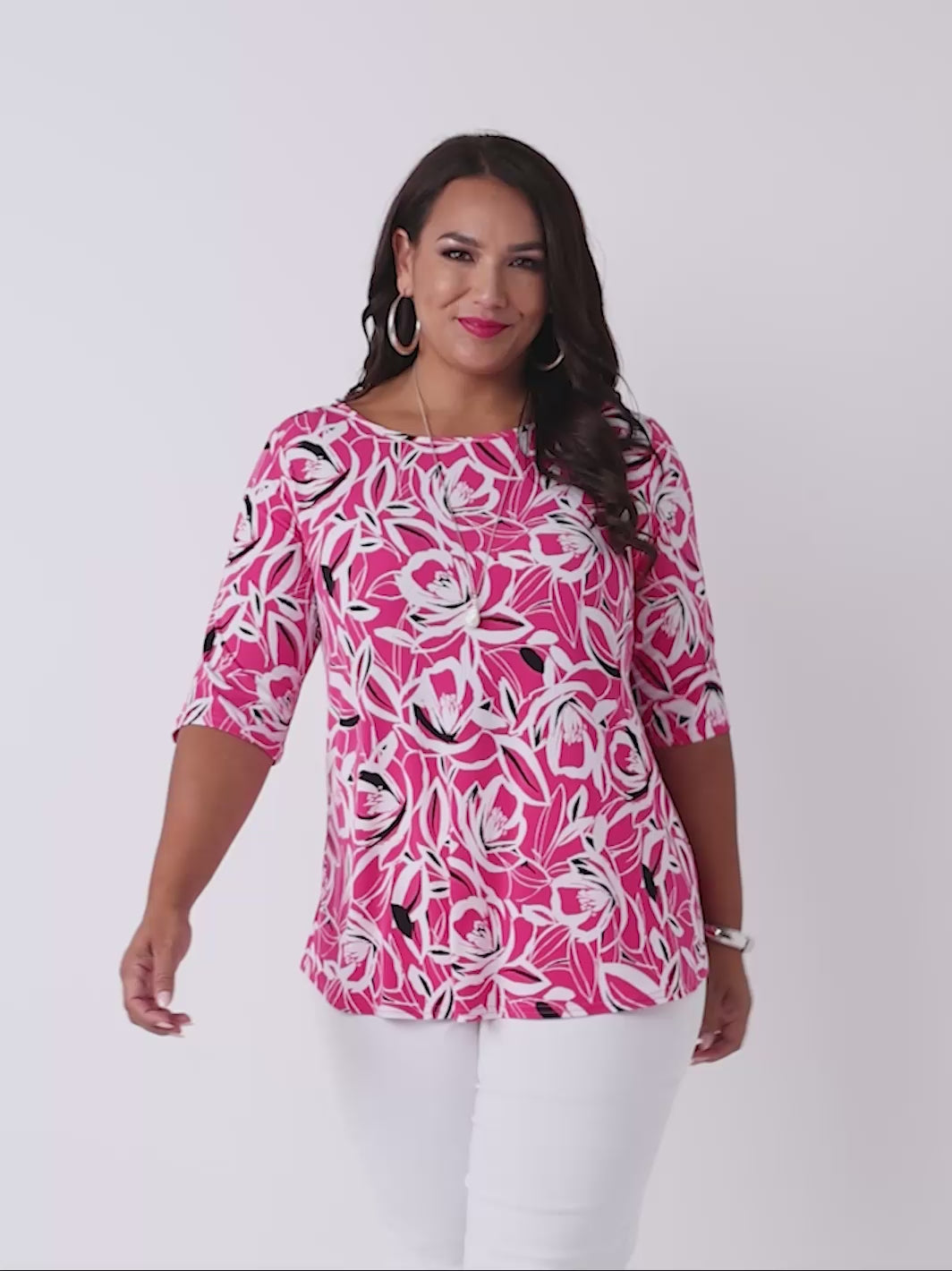 video of a woman wearing a bright pink three-quarter sleeve top with a bold floral print pattern, paired with white pants