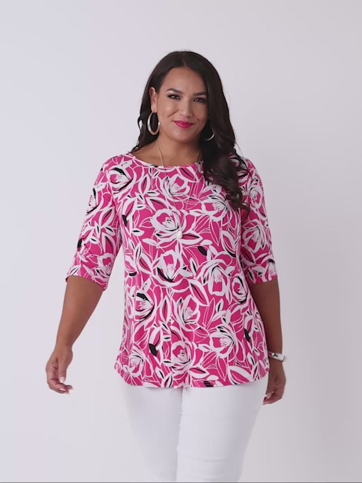 video of a woman wearing a bright pink three-quarter sleeve top with a bold floral print pattern, paired with white pants