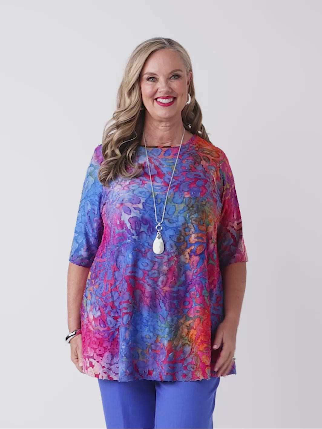 video of woman wearing a colourful swing jersey top with blue and pink tone print with burnout detail, paired with blue pants