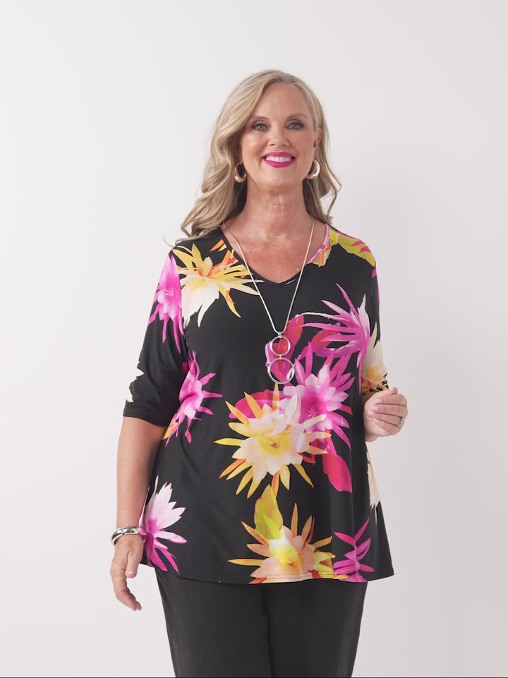 video of model wearing a black short-sleeve V-neck top with a vibrant tropical floral print in pink and yellow