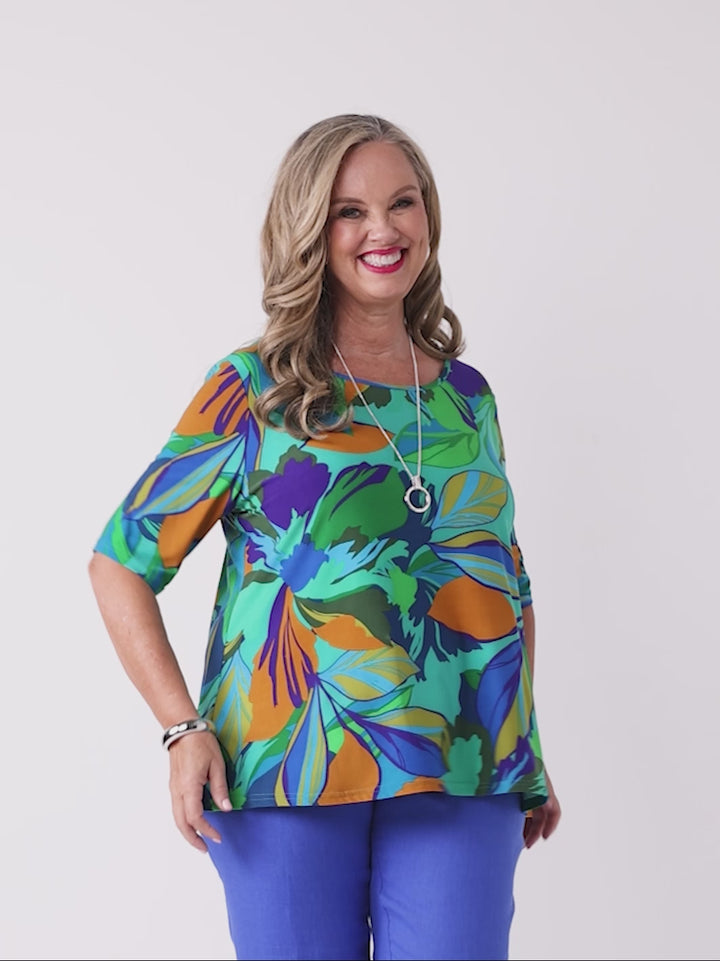 video of model wearing a short-sleeve top with a bold tropical leaf print in green, blue, and orange
