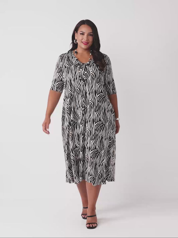 video of model wearing a black, white, and brown zebra-print midi dress with three-quarter sleeves and side pockets