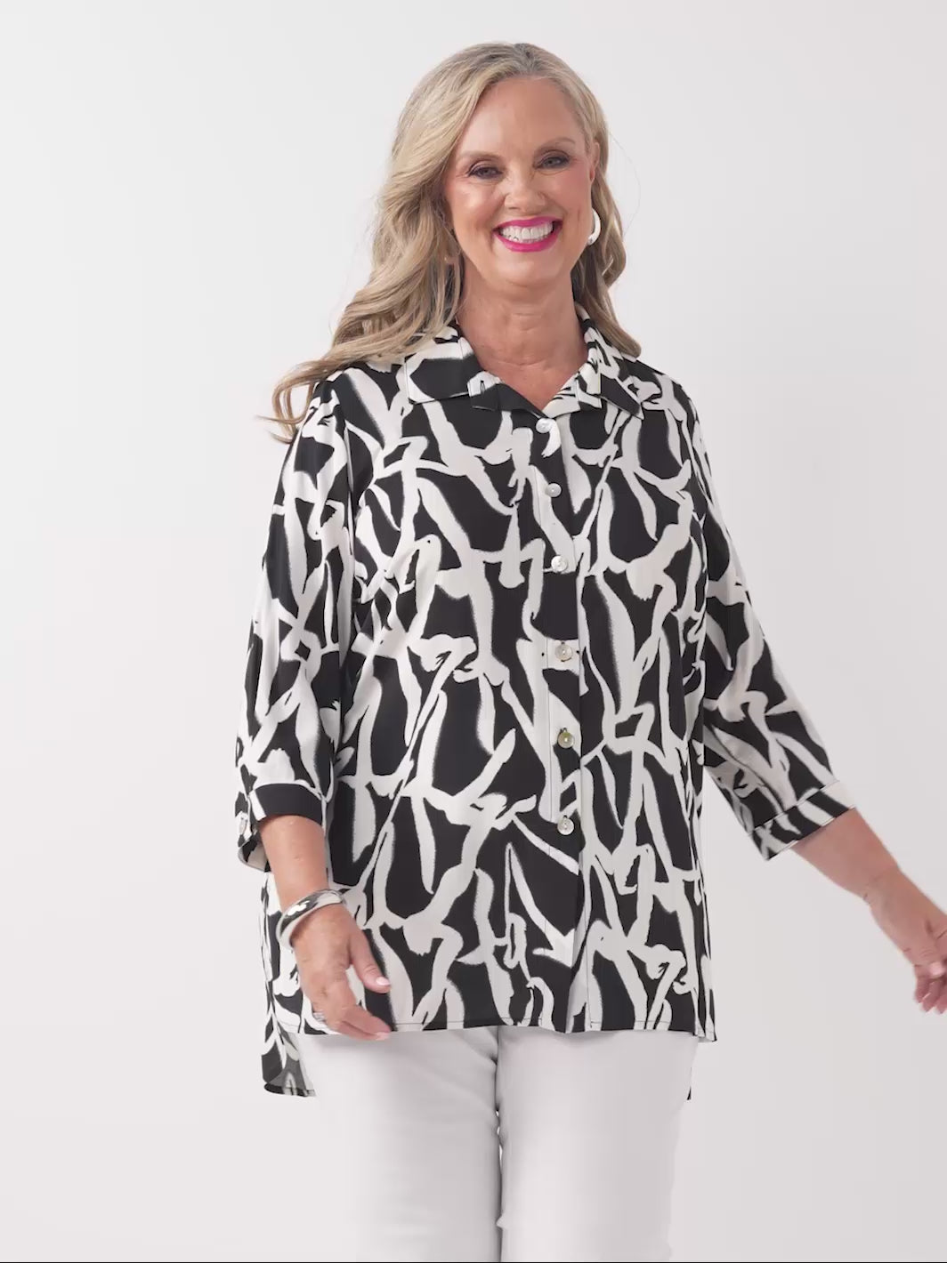 video of model wearing a black and white abstract printed button-up shirt with three-quarter sleeves and white pants