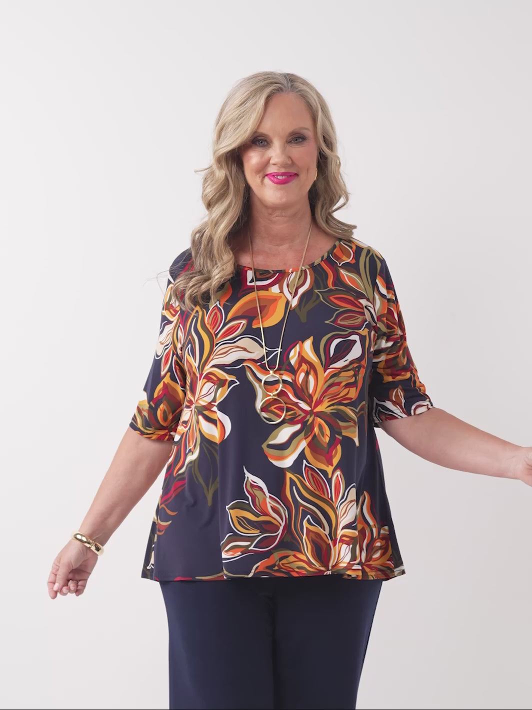 video of model wearing a short-sleeve boat-neck top with a vibrant orange floral print on a navy blue background