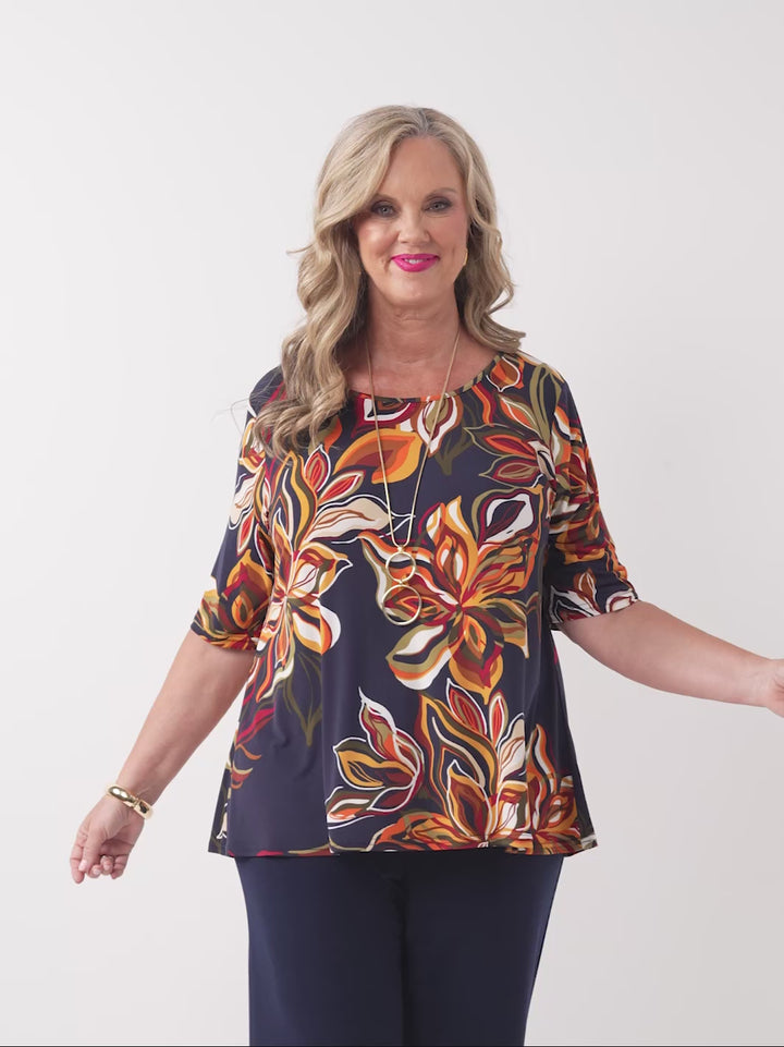 video of model wearing a short-sleeve boat-neck top with a vibrant orange floral print on a navy blue background